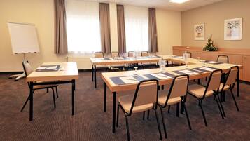 Uma sala de conferências com uma mesa comprida, cadeiras, um quadro branco e uma janela com cortinas.