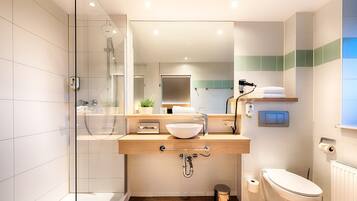 Un baño moderno con ducha envuelta en vidrio, tocador de madera con lavabo y retrete.