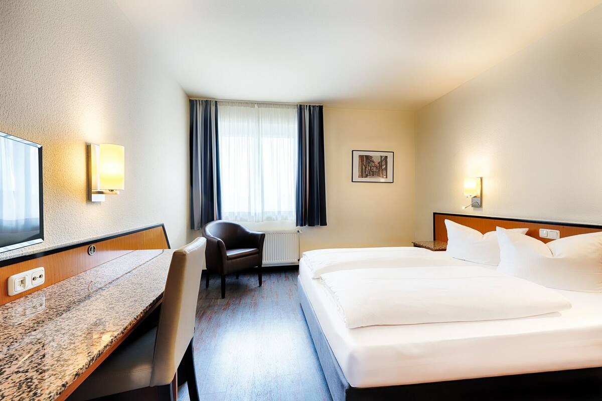 A hotel room with a bed, a desk, a chair, a television, and a window with curtains.