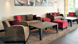 Una sala moderna con un sofá, una mesa de centro y un reposapiés rojo. Hay un cuadro en la pared y una lámpara en la mesita auxiliar.