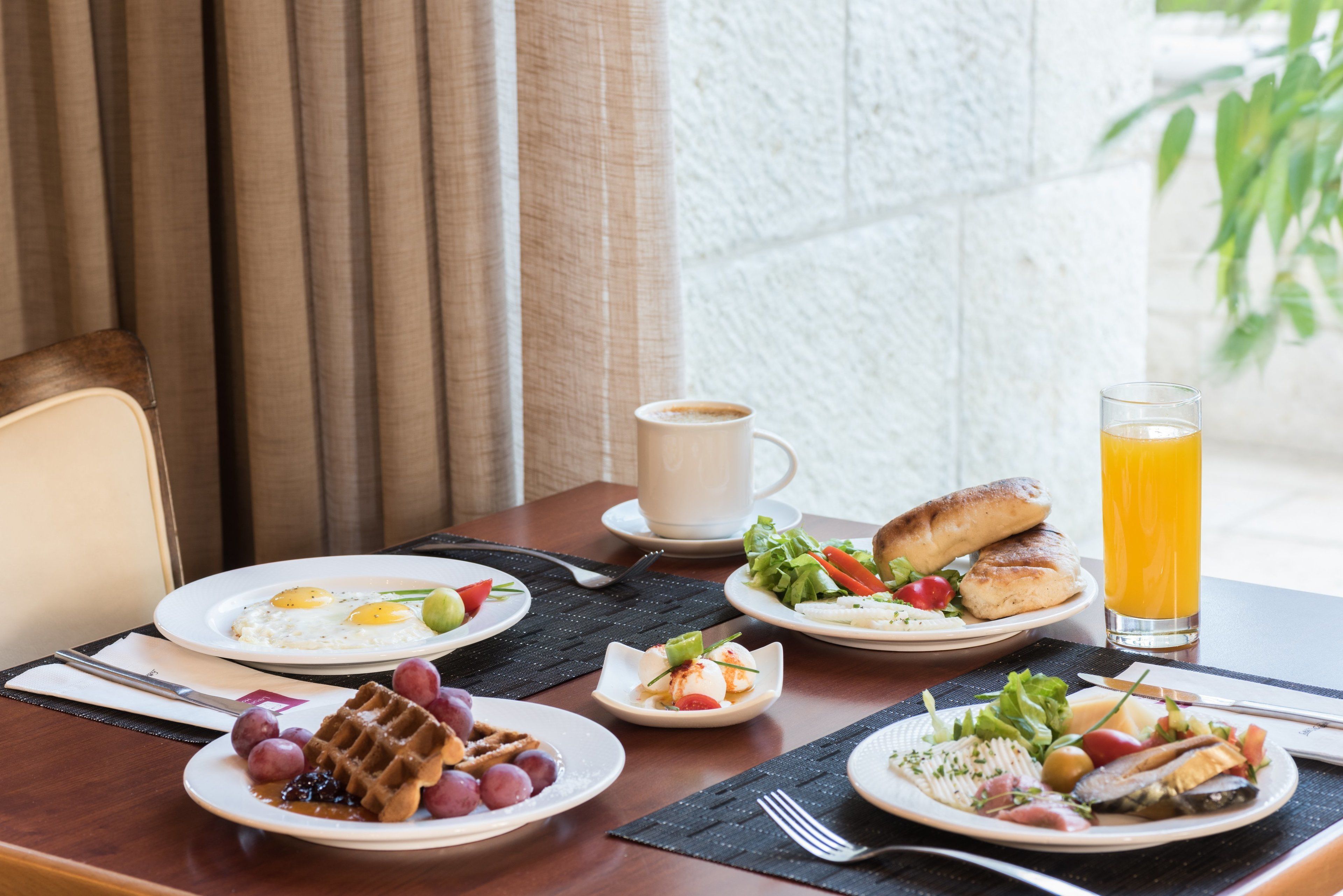 A breakfast table with waffles, eggs, toast, and a glass of orange juice.