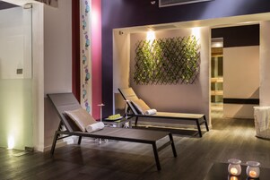 Un spa moderno con dos sillones reclinables, una planta en la pared y una mesita con una bandeja de frutas.