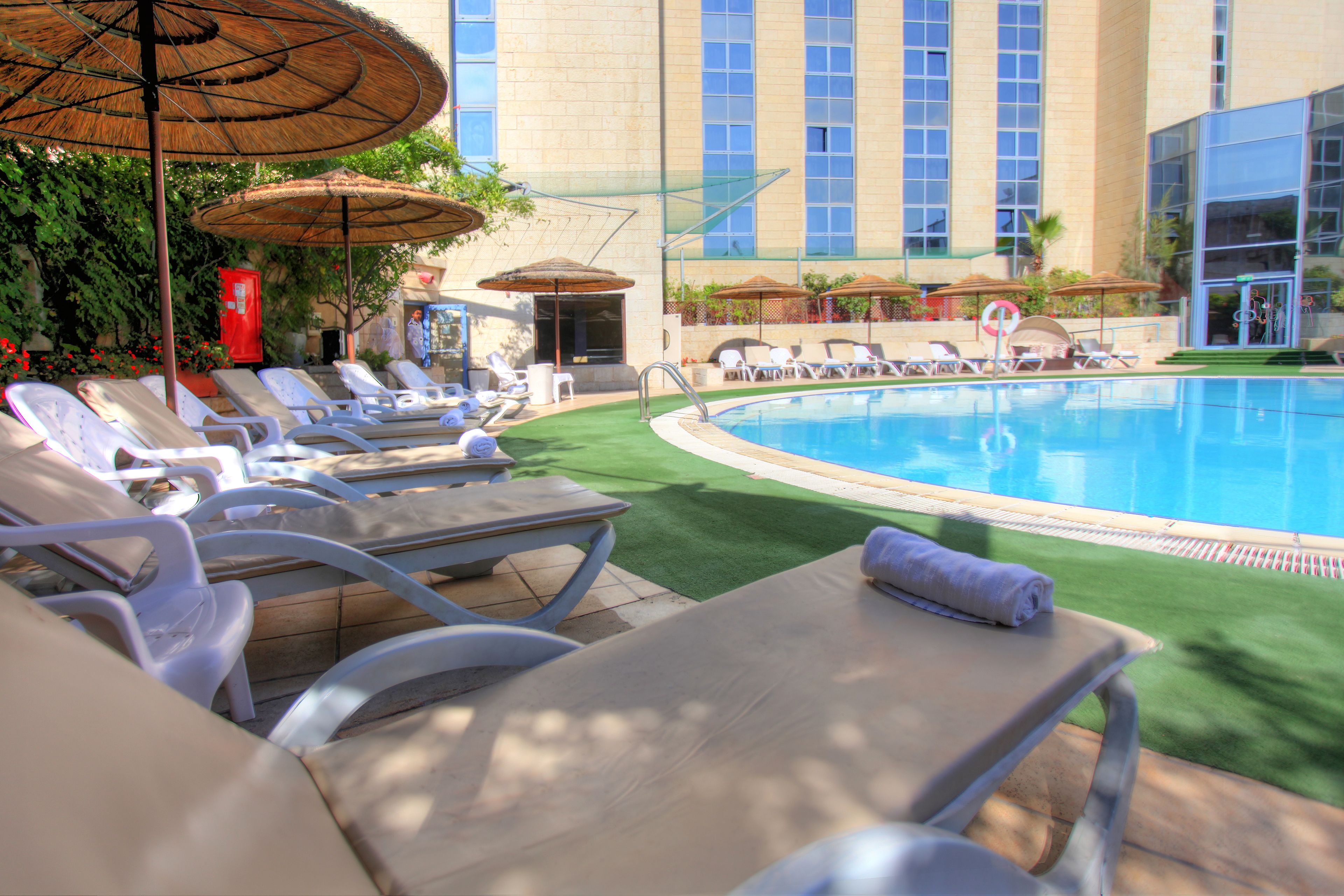 A poolside area with lounge chairs and umbrellas, a clear blue pool, and a building with large windows in the background.