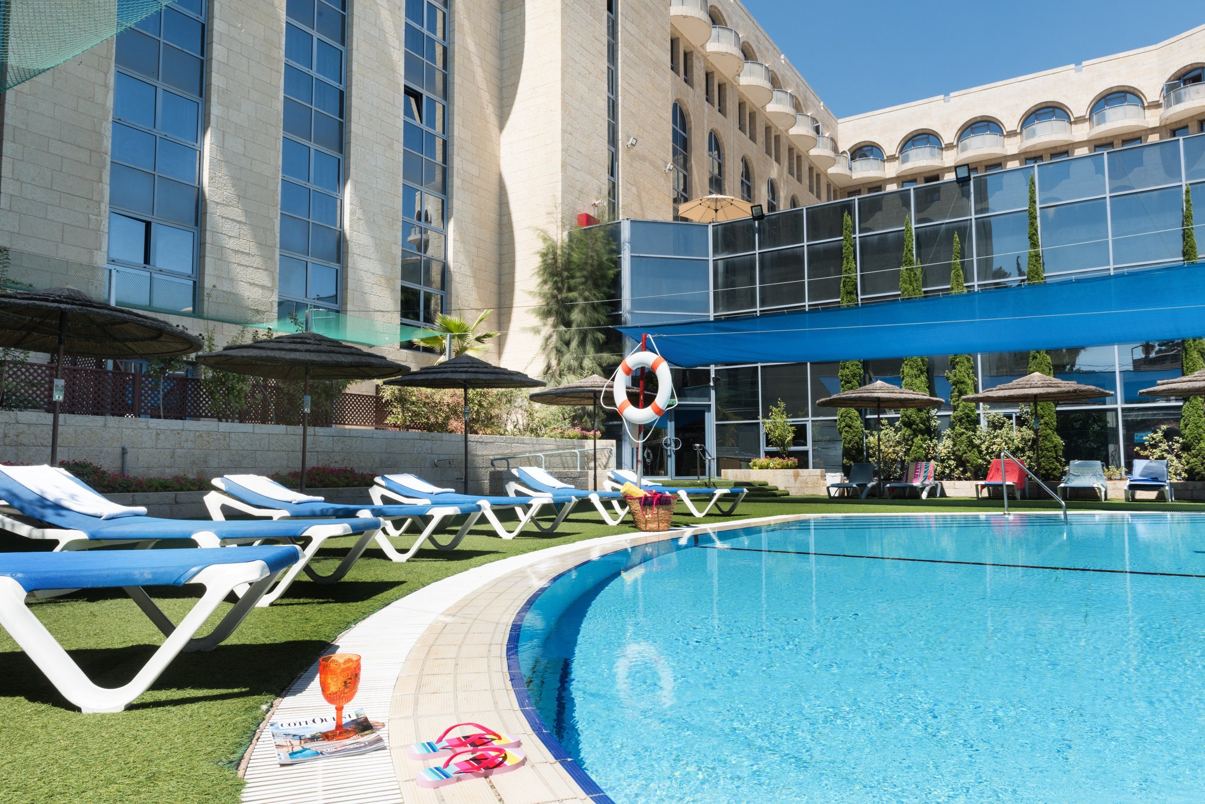 A swimming pool with lounge chairs and umbrellas, a lifebuoy, and a building with large windows and balconies.