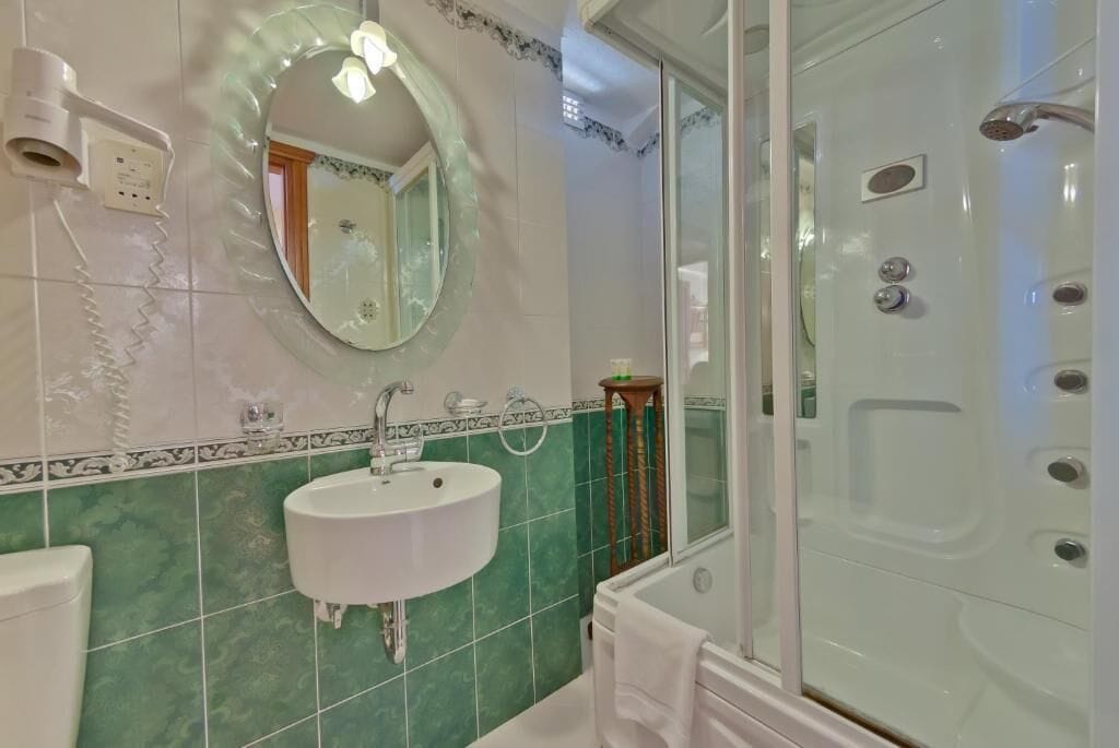 A bathroom with a white sink, a mirror, a shower with multiple nozzles, and green-tiled walls.