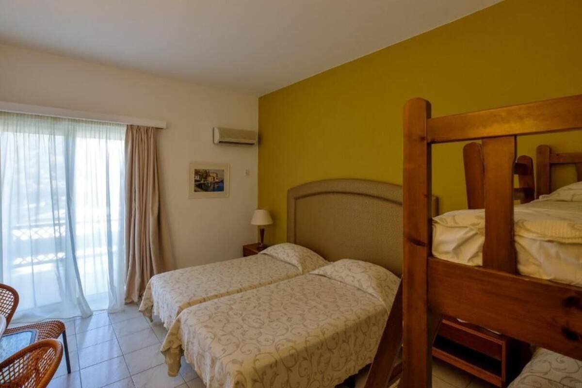 A hotel room with two single beds, a wooden headboard, a small table with a chair, and a window with curtains.