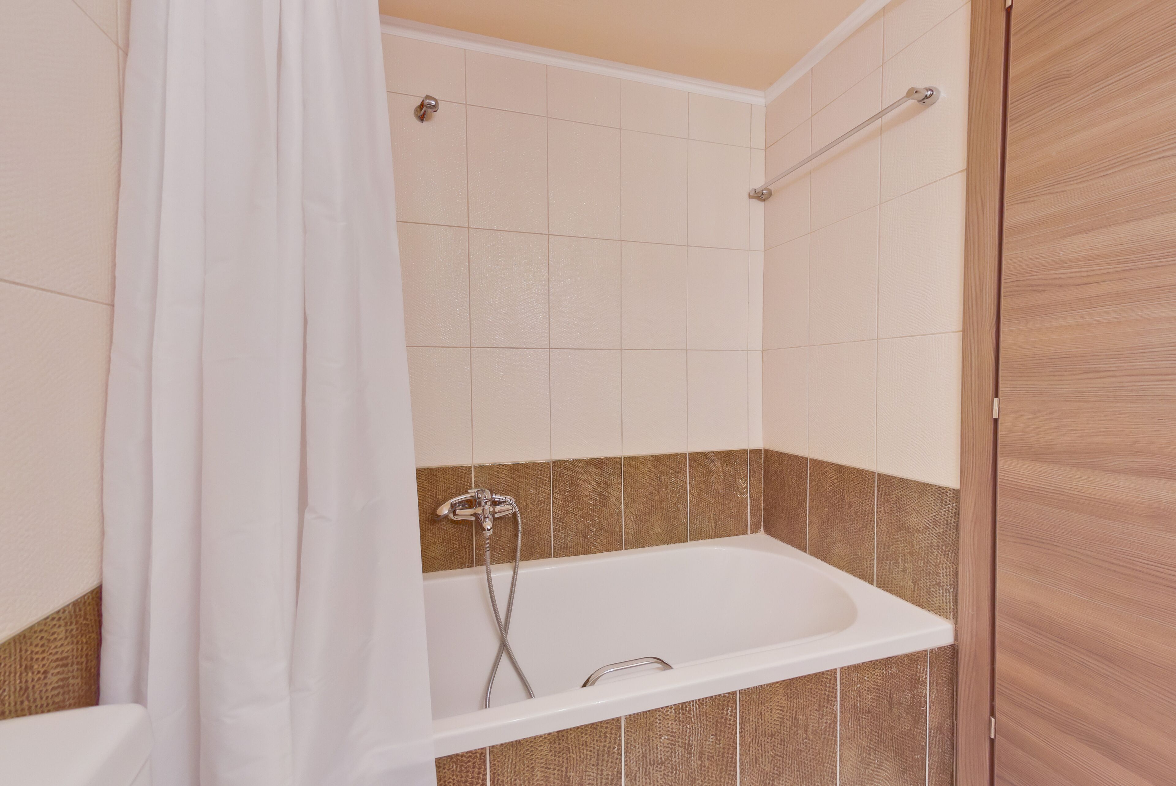 A modern bathroom with a bathtub, shower, and a wooden door.