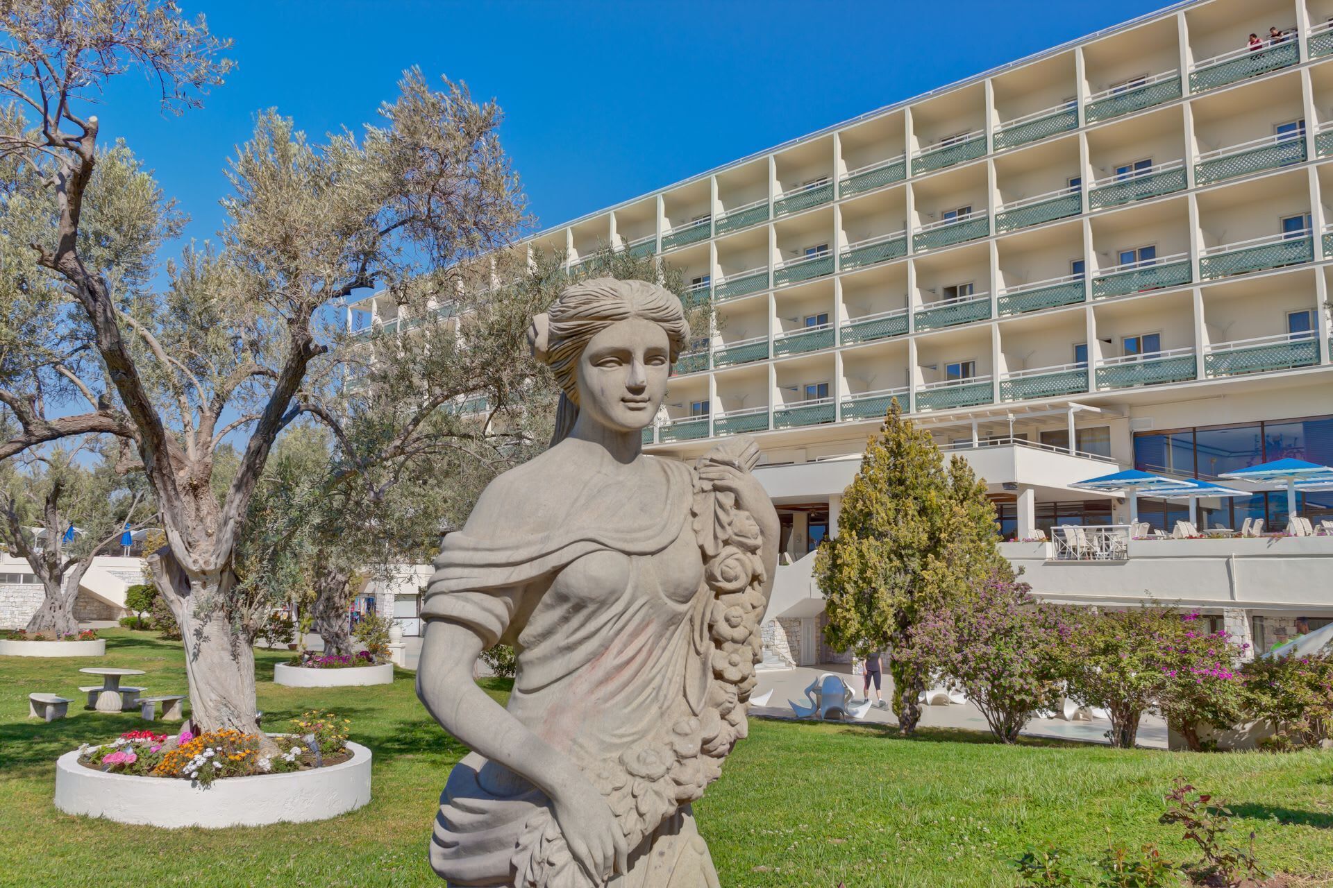 A statue in a landscaped area with a hotel building in the background.