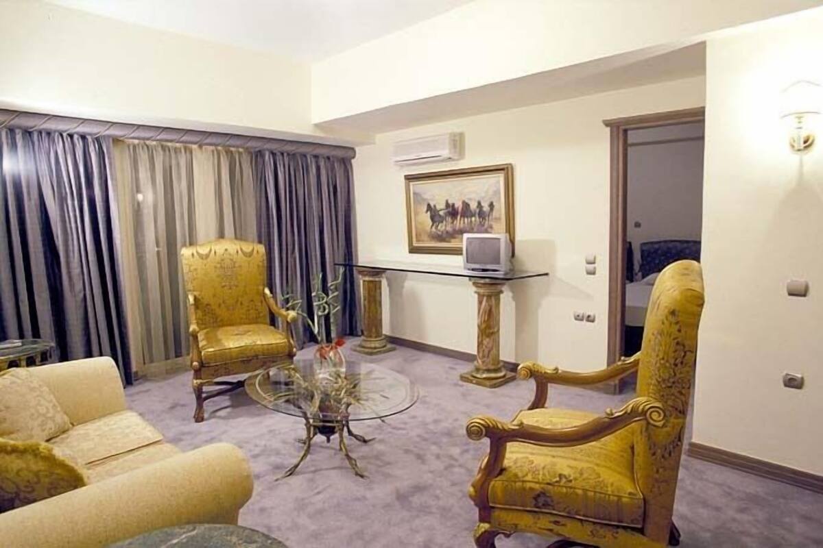 A room with a sofa, two armchairs, a glass coffee table, a small side table, and a painting on the wall.