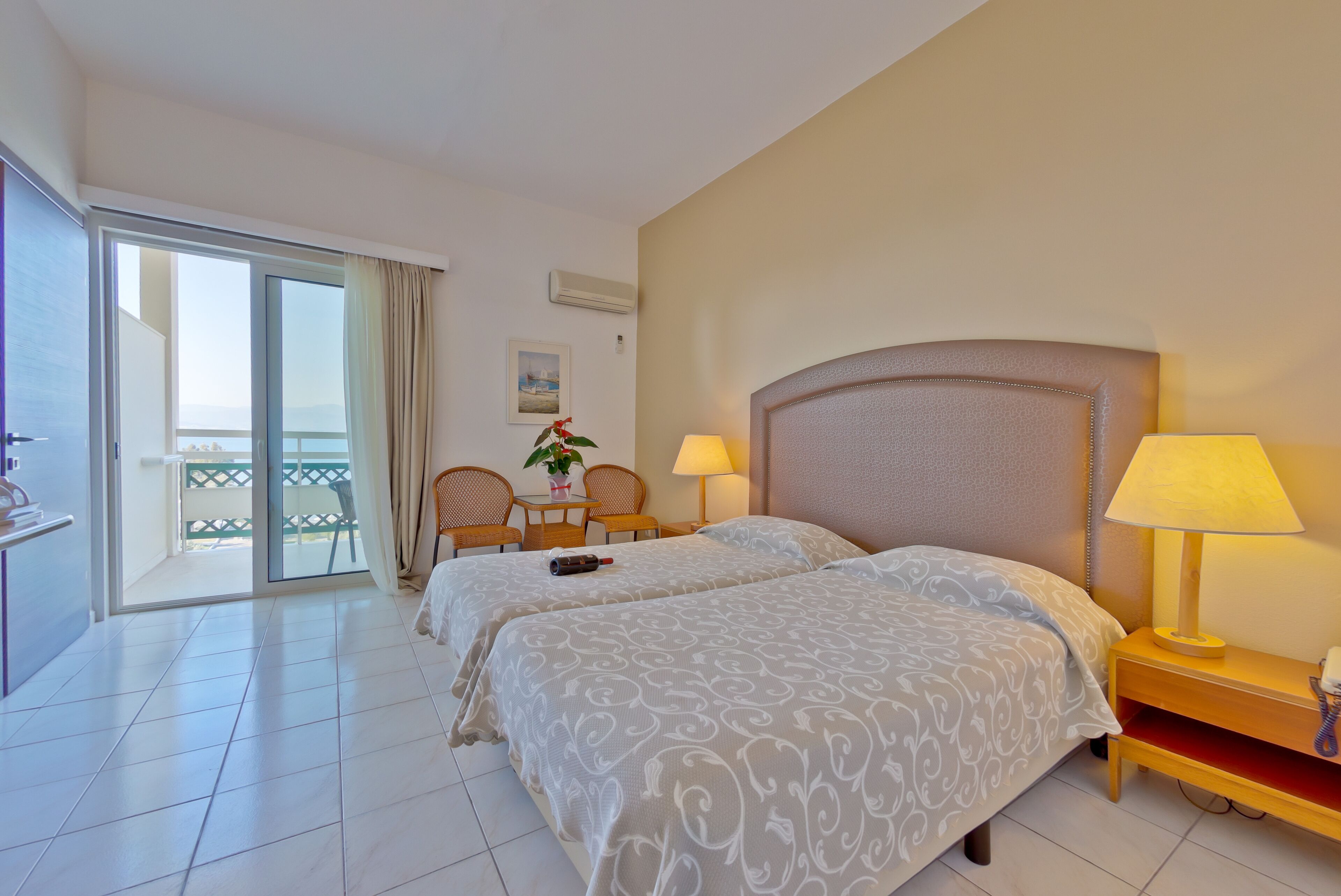 Una habitación de hotel con dos camas, un balcón, una mesita con sillas y una lámpara en la mesita de noche.