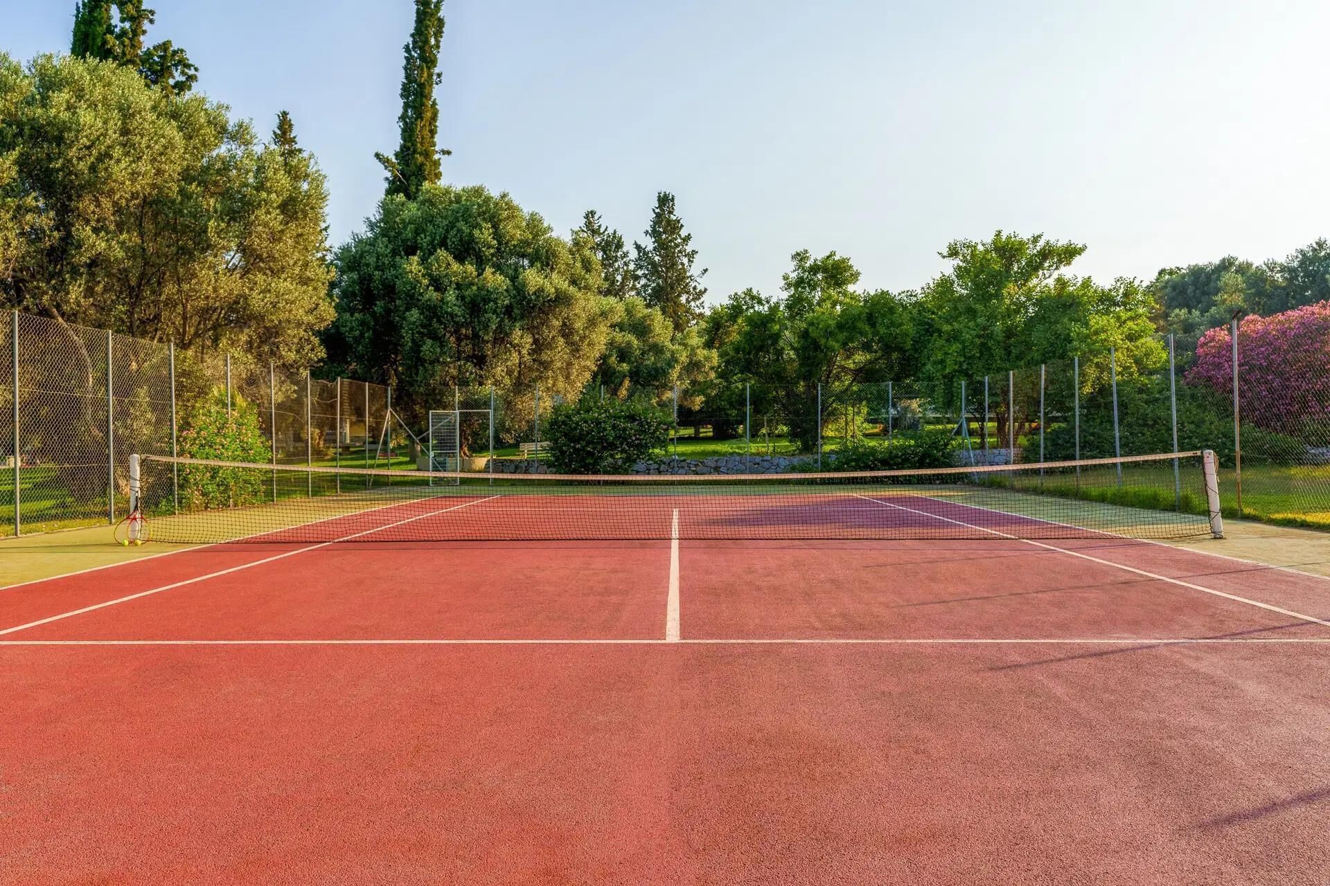 Un court de tennis avec un filet, entouré d’arbres et d’une clôture.