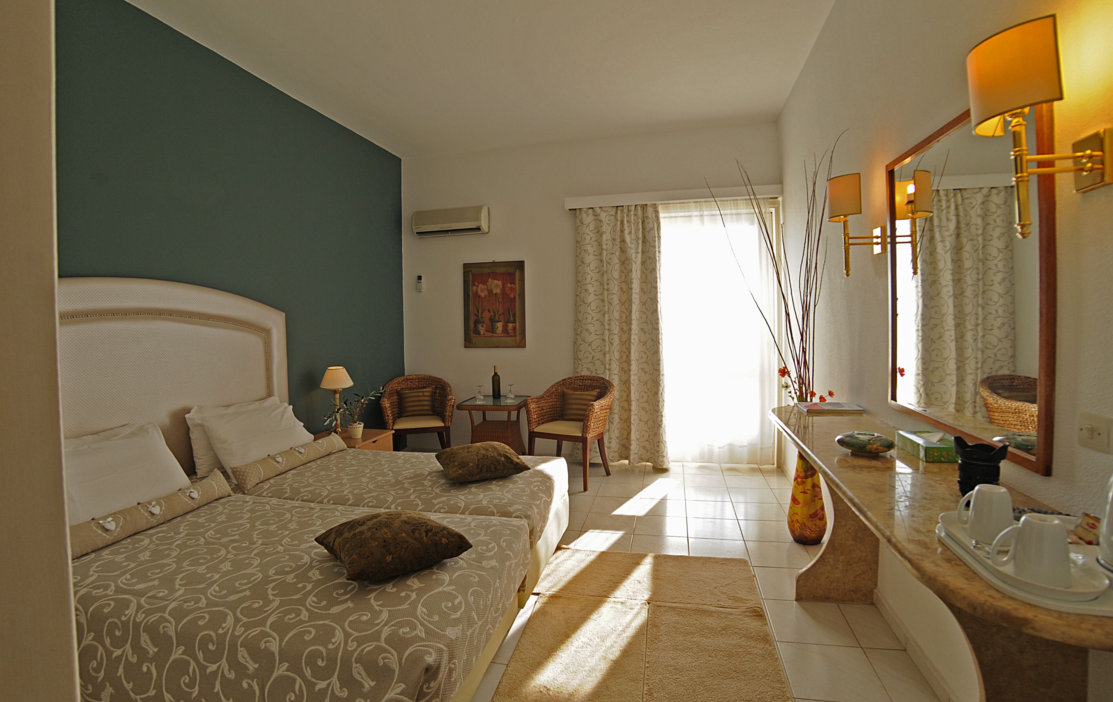 Habitación de hotel con dos camas, una zona de estar con una mesa y sillas, un espejo grande y una ventana con cortinas.