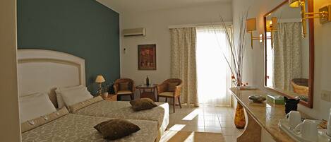 Habitación de hotel con dos camas, una zona de estar con una mesa y sillas, un espejo grande y una ventana con cortinas.