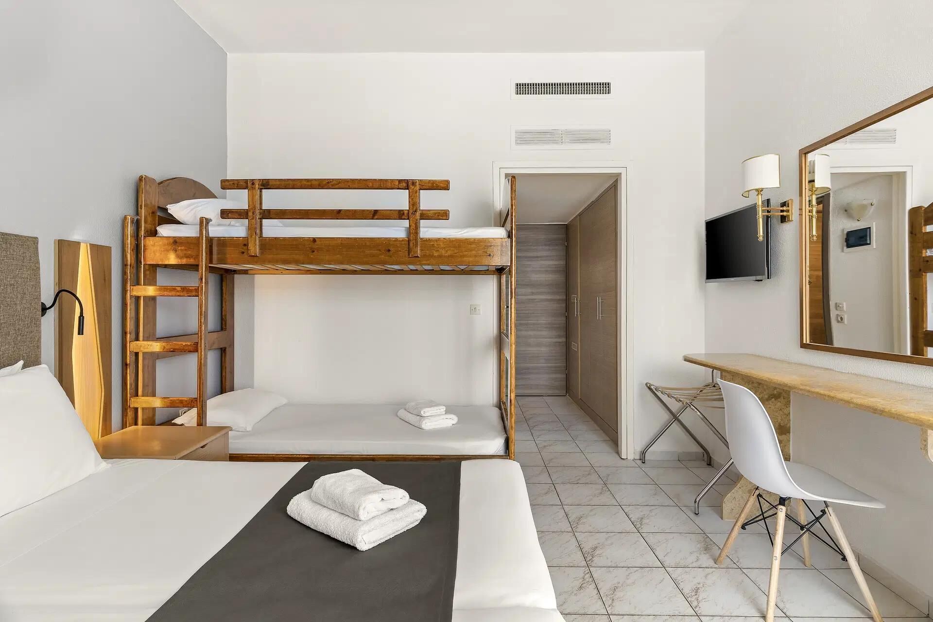 Una camera d'albergo con un letto a castello, una scrivania con una sedia, una televisione e uno specchio.
