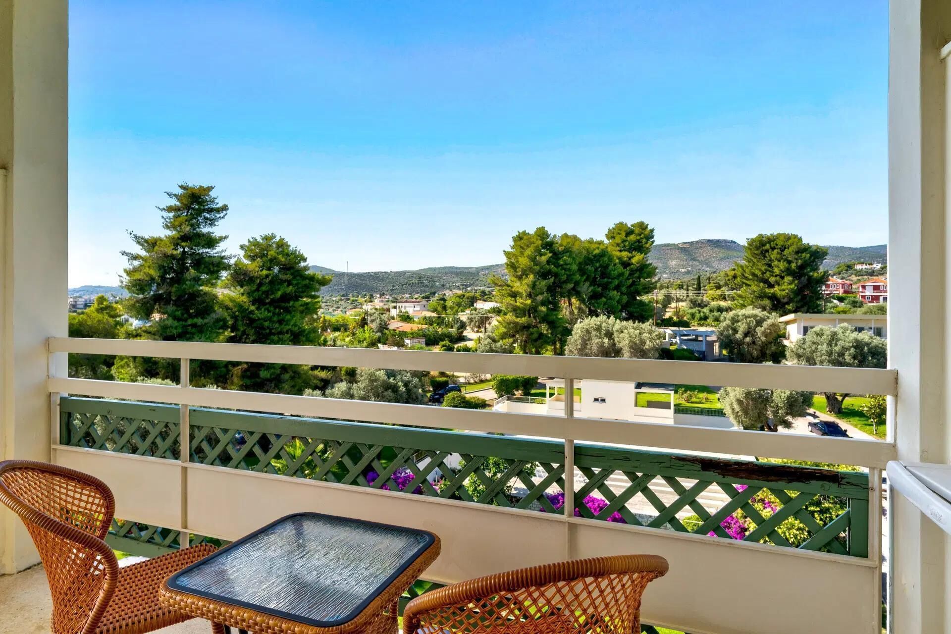 A balcony with wicker furniture and a view of a green landscape with trees and buildings.
