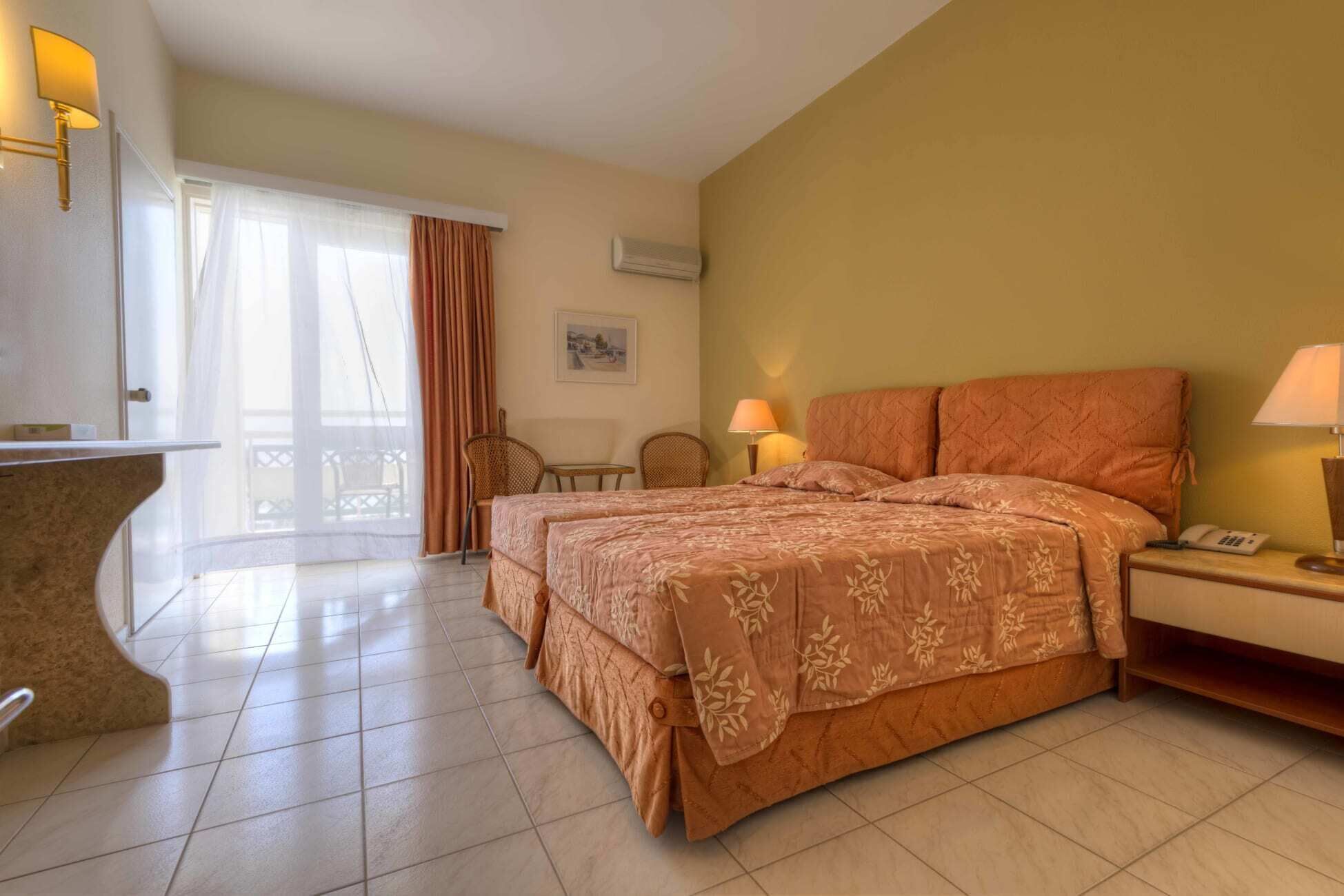Una habitación de hotel con una cama, dos sillas, un escritorio, una lámpara y un cuadro en la pared.