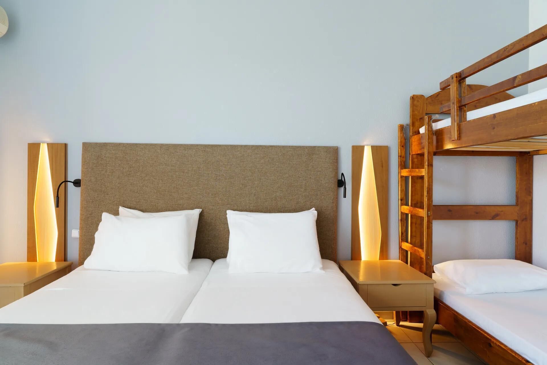 A double bed with a wooden headboard, two bedside tables, and a wooden bunk bed to the right.