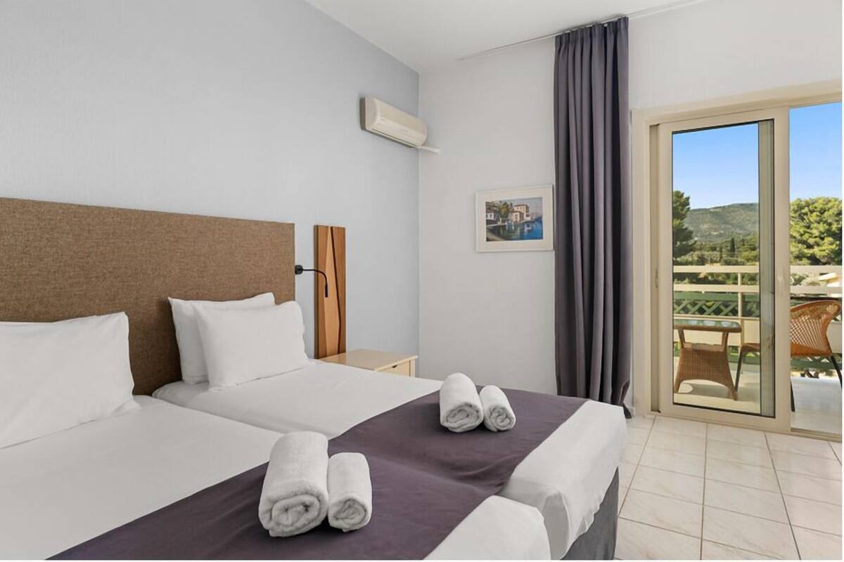 A hotel room with two beds, a balcony with a table and chairs, and a picture on the wall.