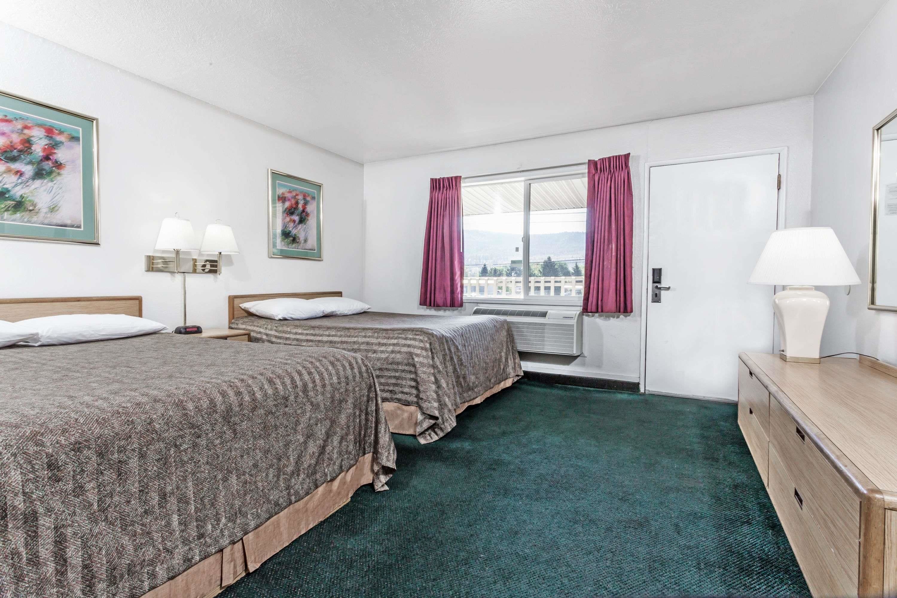 Une chambre d’hôtel avec deux lits, une fenêtre avec des rideaux, un bureau avec une lampe et une vue sur la ville.