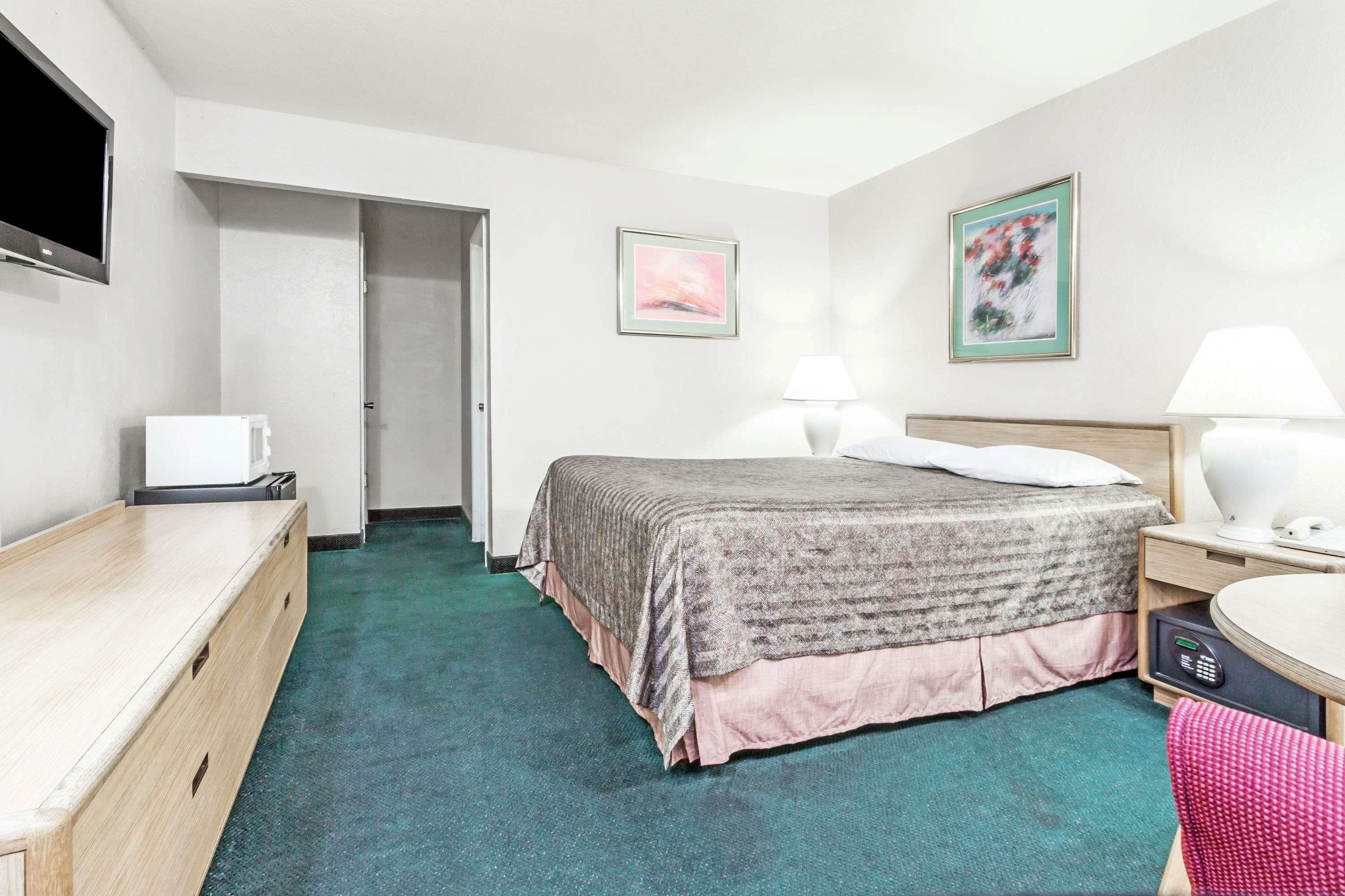 Une chambre d’hôtel équipée d’un lit, de tables de chevet, d’un bureau, d’une chaise, d’une télévision et d’œuvres d’art accrochées aux murs.