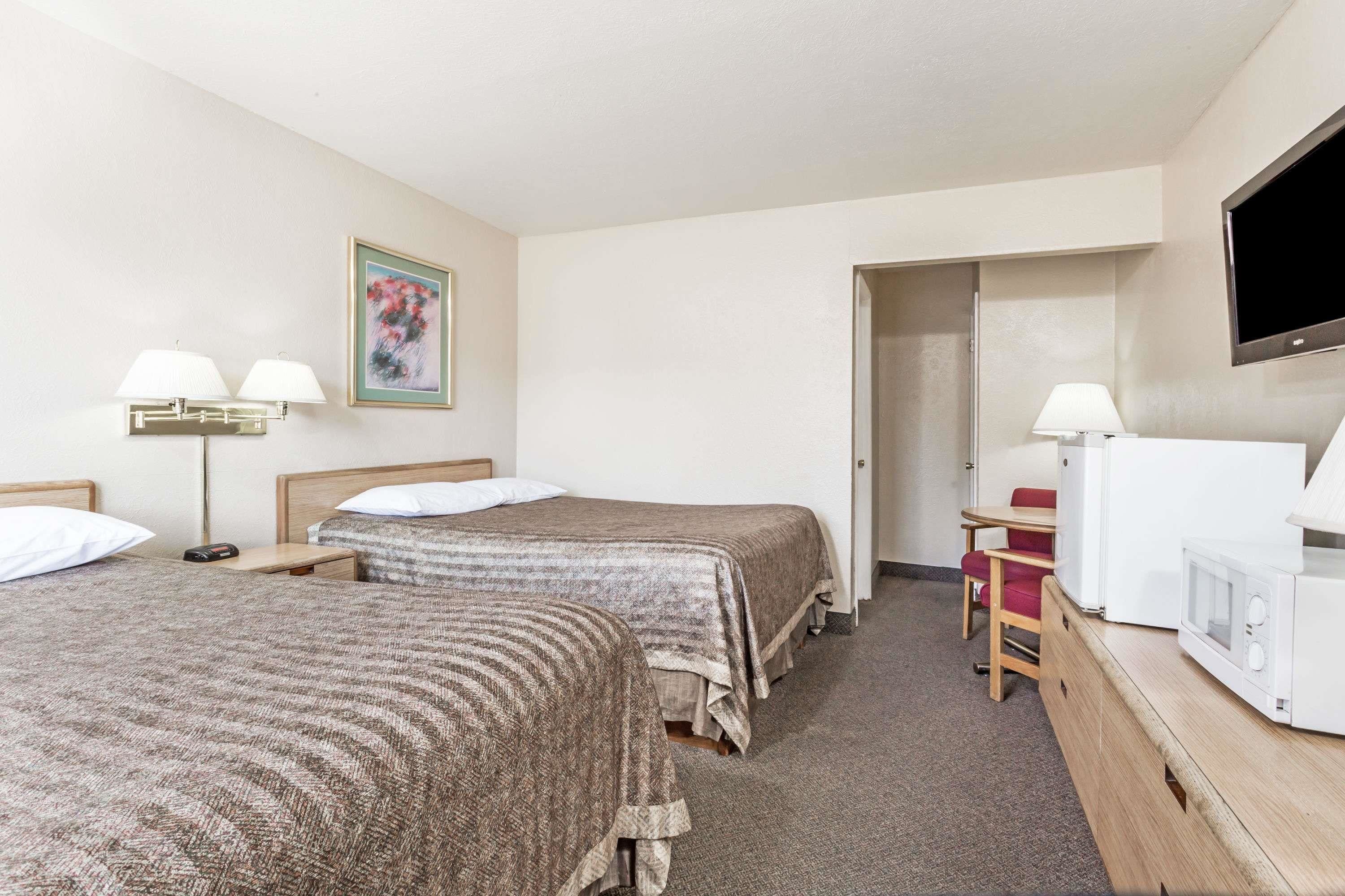 A hotel room with two beds, a desk, a chair, a television, and a microwave.