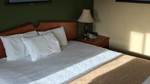 A hotel room with a large bed, two framed pictures on the walls, a bedside lamp, and a nightstand with a phone. - Travelodge by Wyndham La Grande (La Grande)