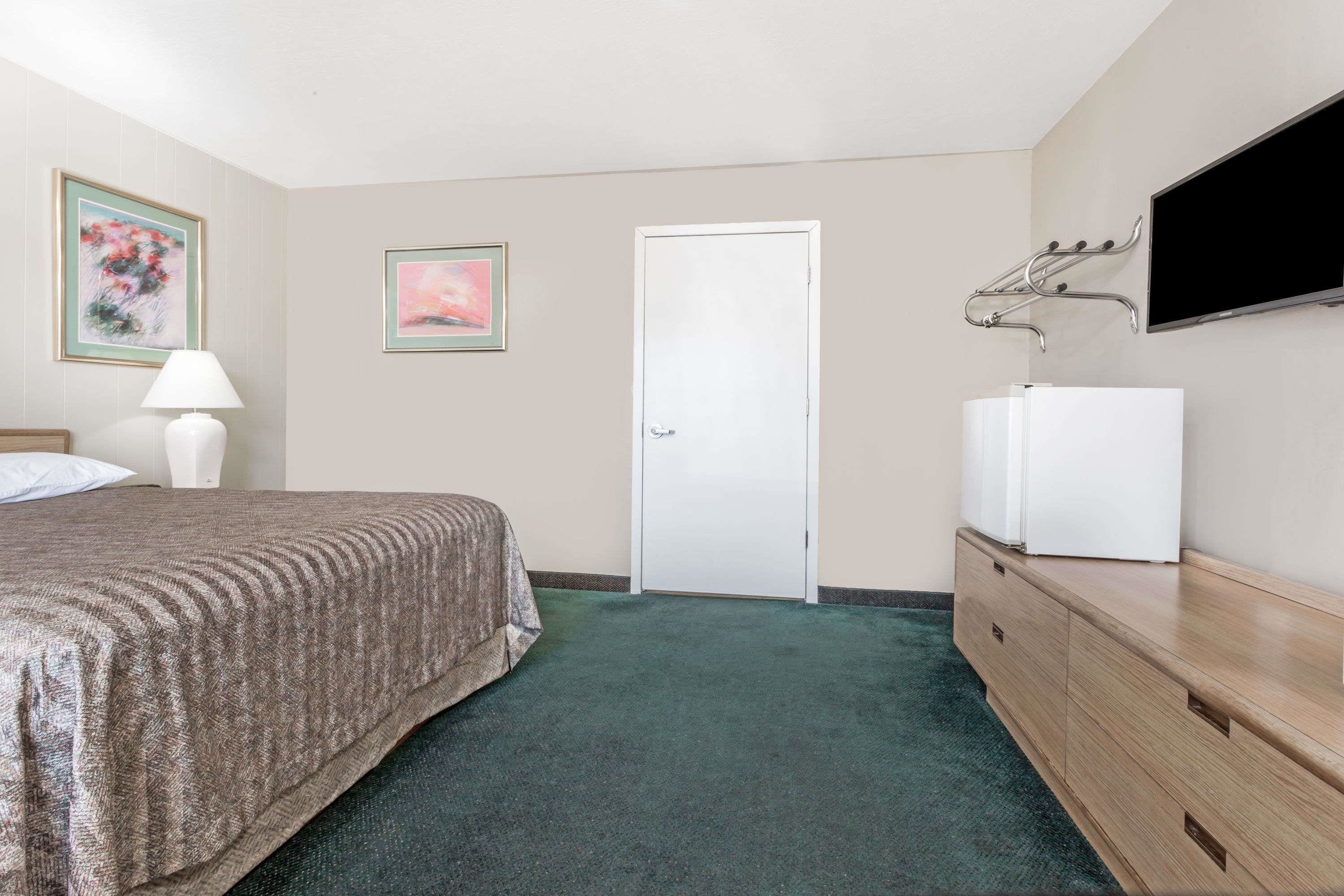 Une chambre à coucher avec un lit, une commode, un téléviseur fixé au mur et une porte.