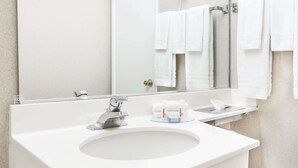 A modern bathroom with a white sink, a mirror, and a towel rack with multiple towels. - Travelodge by Wyndham La Grande (La Grande)