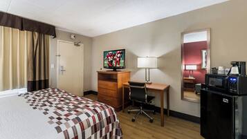 Una habitación de hotel con una cama, un escritorio, una silla, un televisor, una cafetera y un microondas.