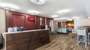 Zona de recepción de un hotel con un mostrador de madera, un quiosco digital y un cartel que indica Wi-Fi gratuito en todas las habitaciones.