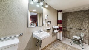Baño con lavamanos blanco, espejo y ducha. Hay un perchero y un secamanos.
