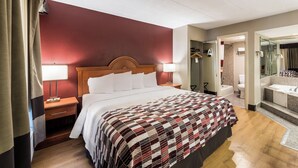 Habitación de hotel con cama, mesitas de noche, un espejo y un baño visible a través de una puerta abierta.