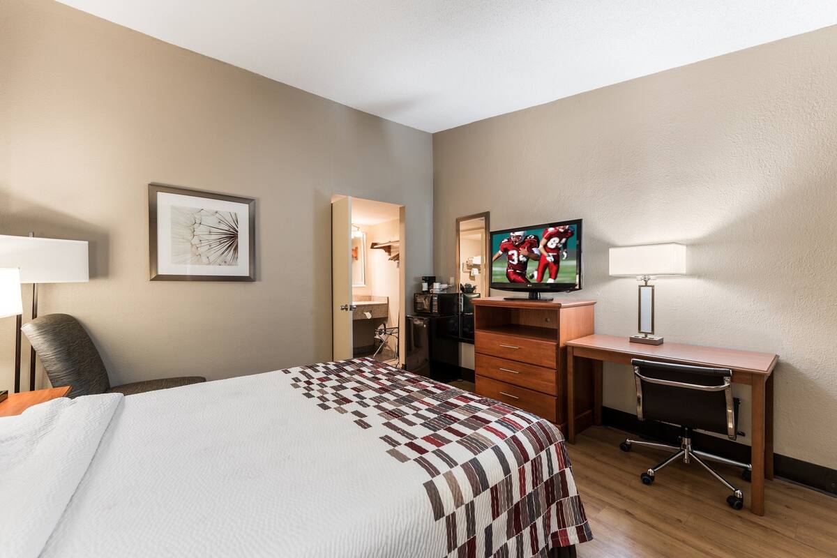 A hotel room with a bed, a desk, a television, and a chair.