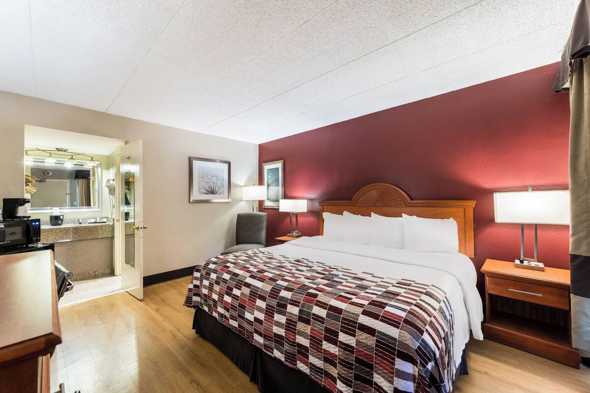 A hotel room with a bed, bedside tables, a desk, a chair, a mirror, and a door leading to a bathroom.