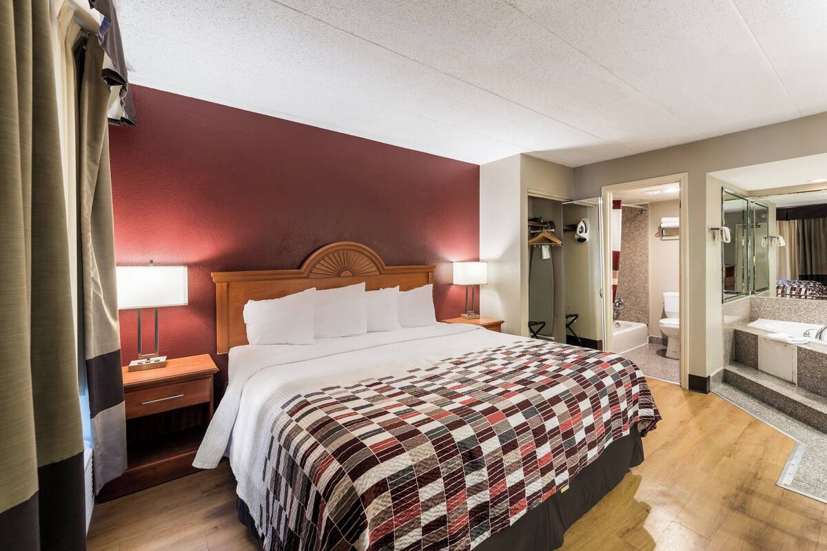 A hotel room with a bed, bedside tables, a mirror, and a bathroom visible through an open door.