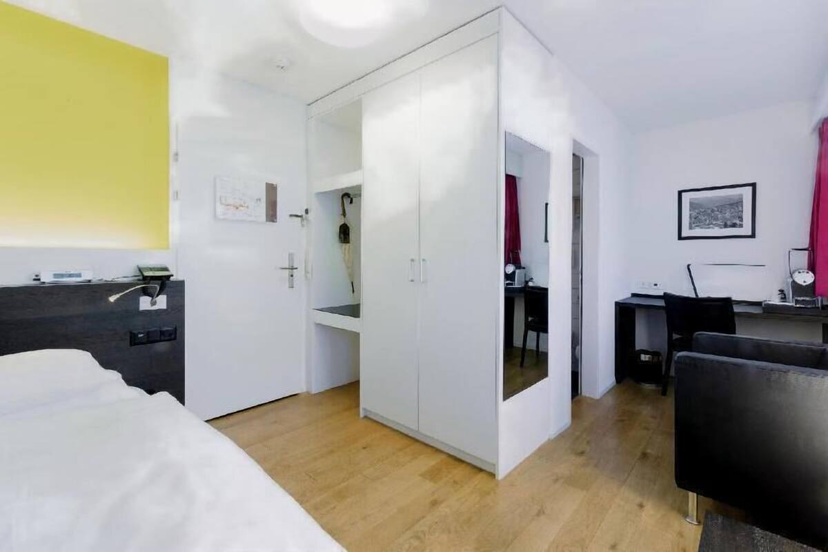 Quarto de hotel com cama, escrivaninha, guarda-roupa e espelho.