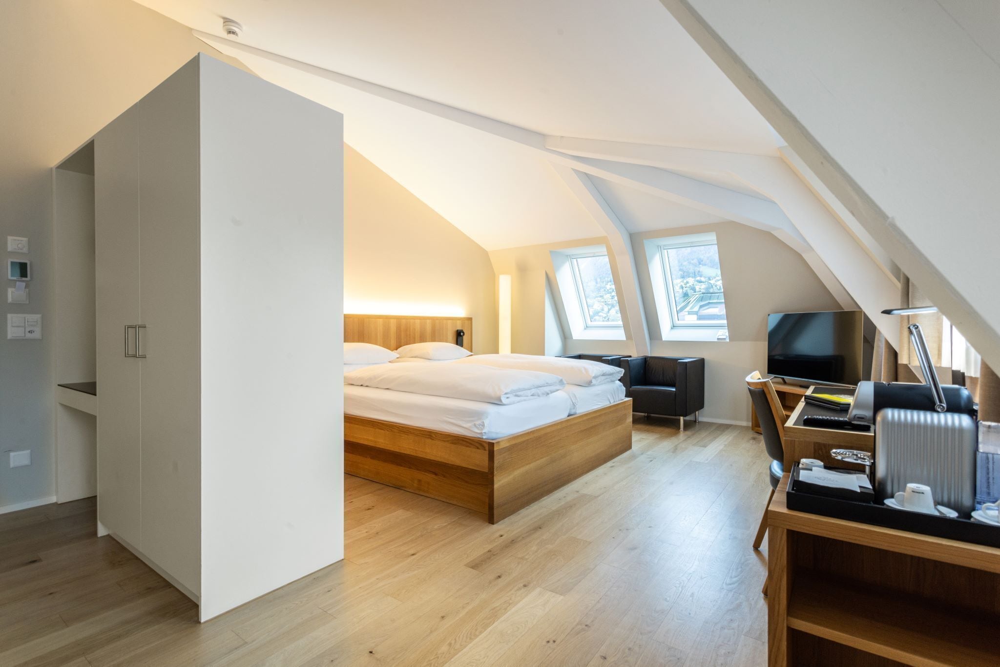 A modern loft bedroom with a large bed, a desk, and a television.