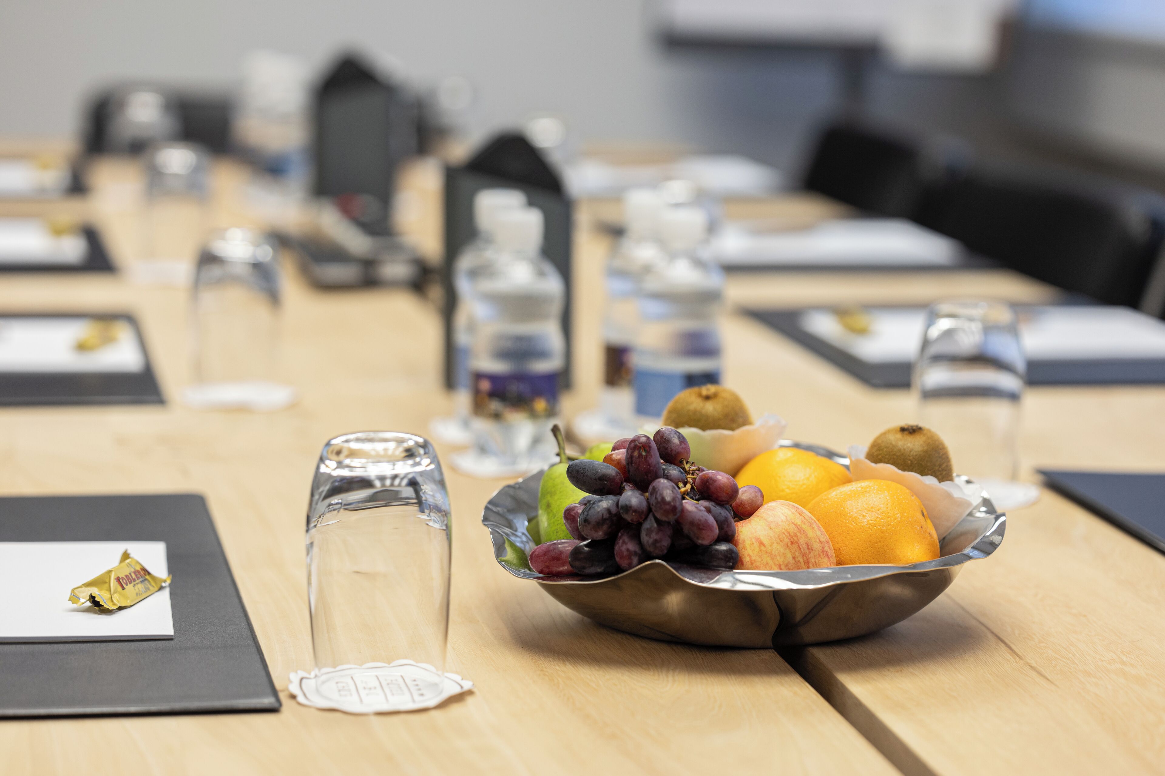 A conference table with a fruit bowl, water bottles, and a glass.