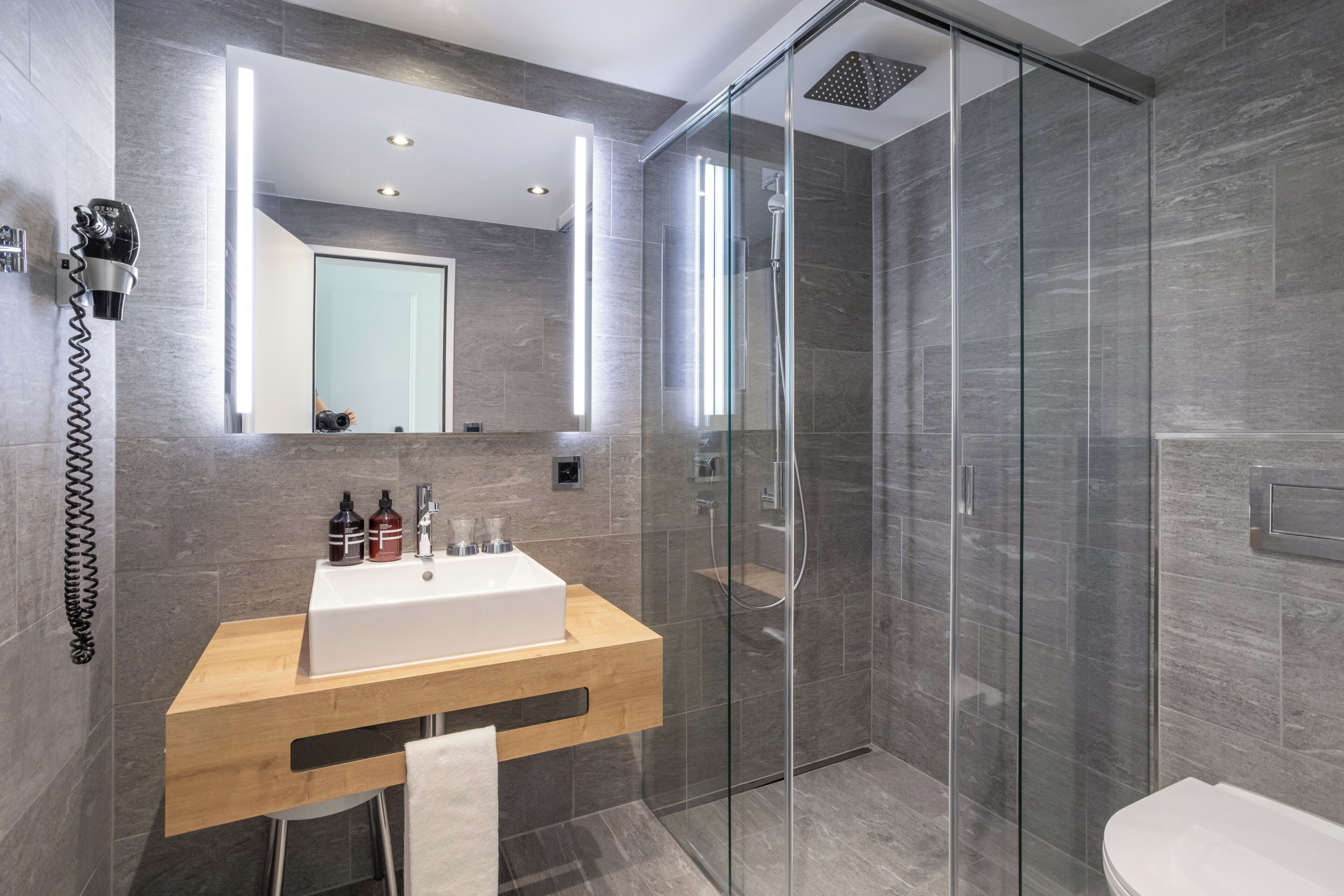 A modern bathroom with a glass-enclosed shower, a wooden vanity with a white sink, and a large mirror above the vanity.