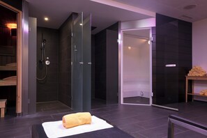 A modern bathroom with a glass-enclosed shower, a wooden bench, and a towel on a mat.