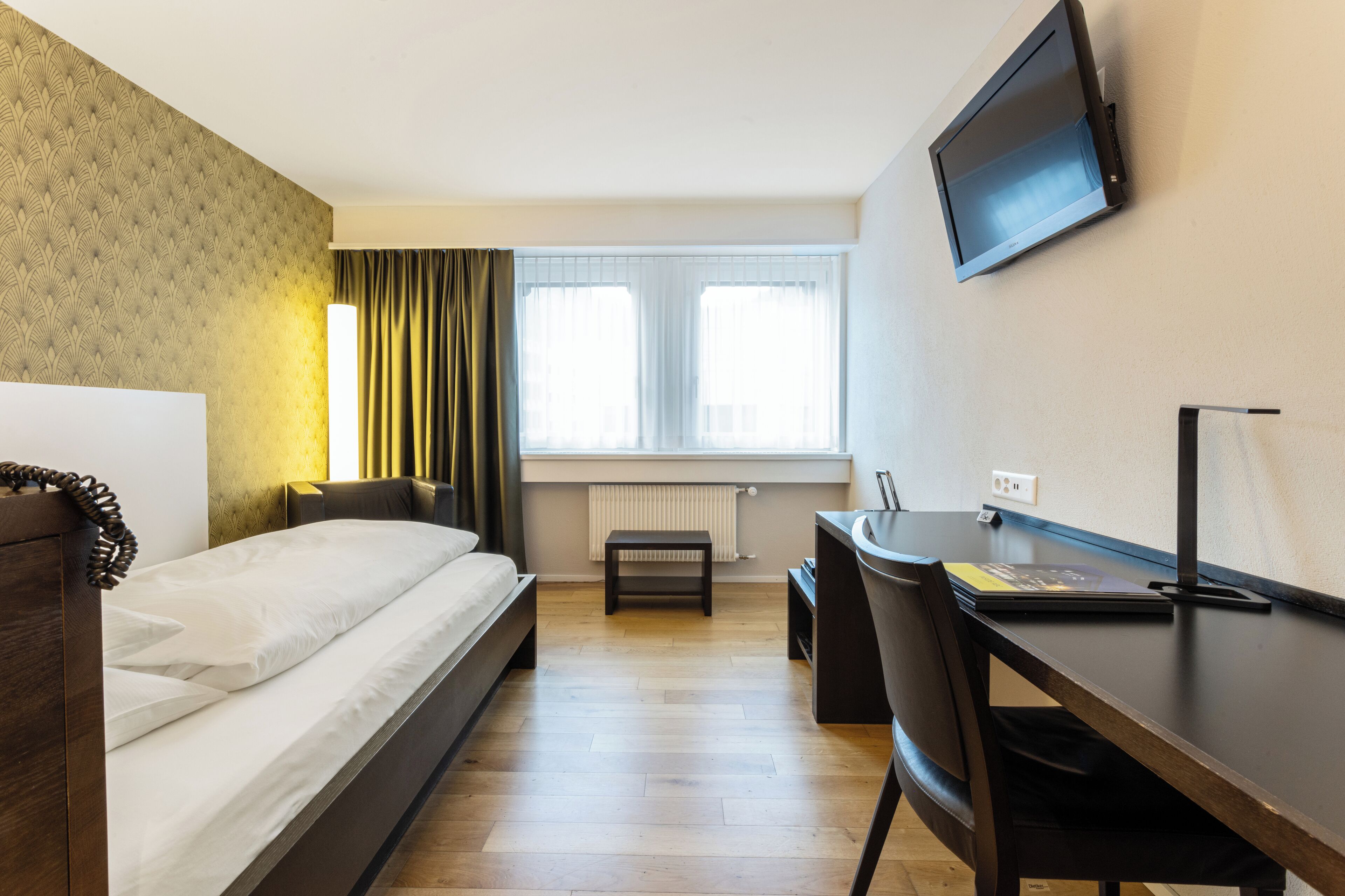 A hotel room with a bed, a desk, a chair, a television, and a window with curtains.