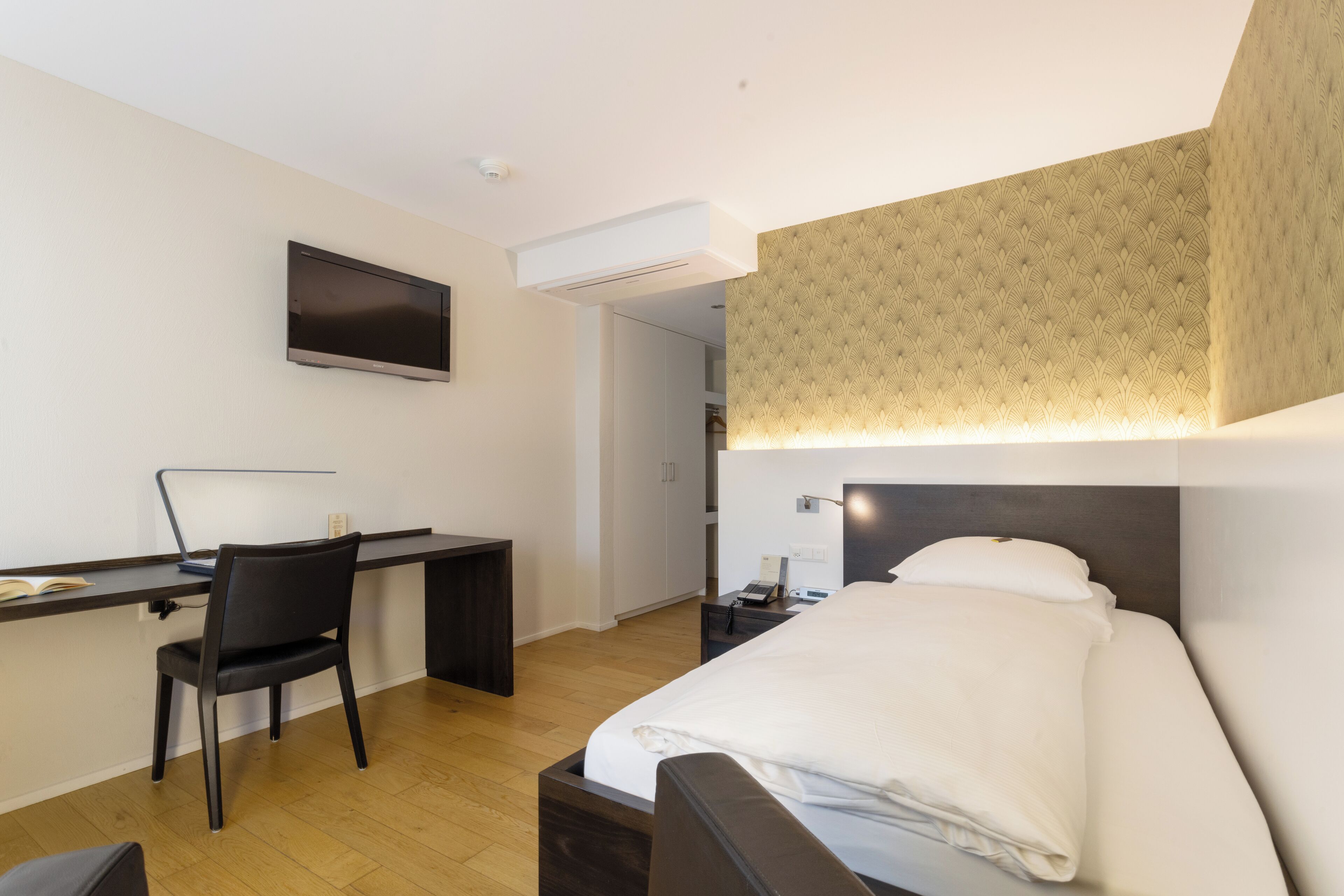 A hotel room with a bed, desk, chair, and a television mounted on the wall.
