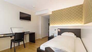 A hotel room with a bed, desk, chair, and a television mounted on the wall.
