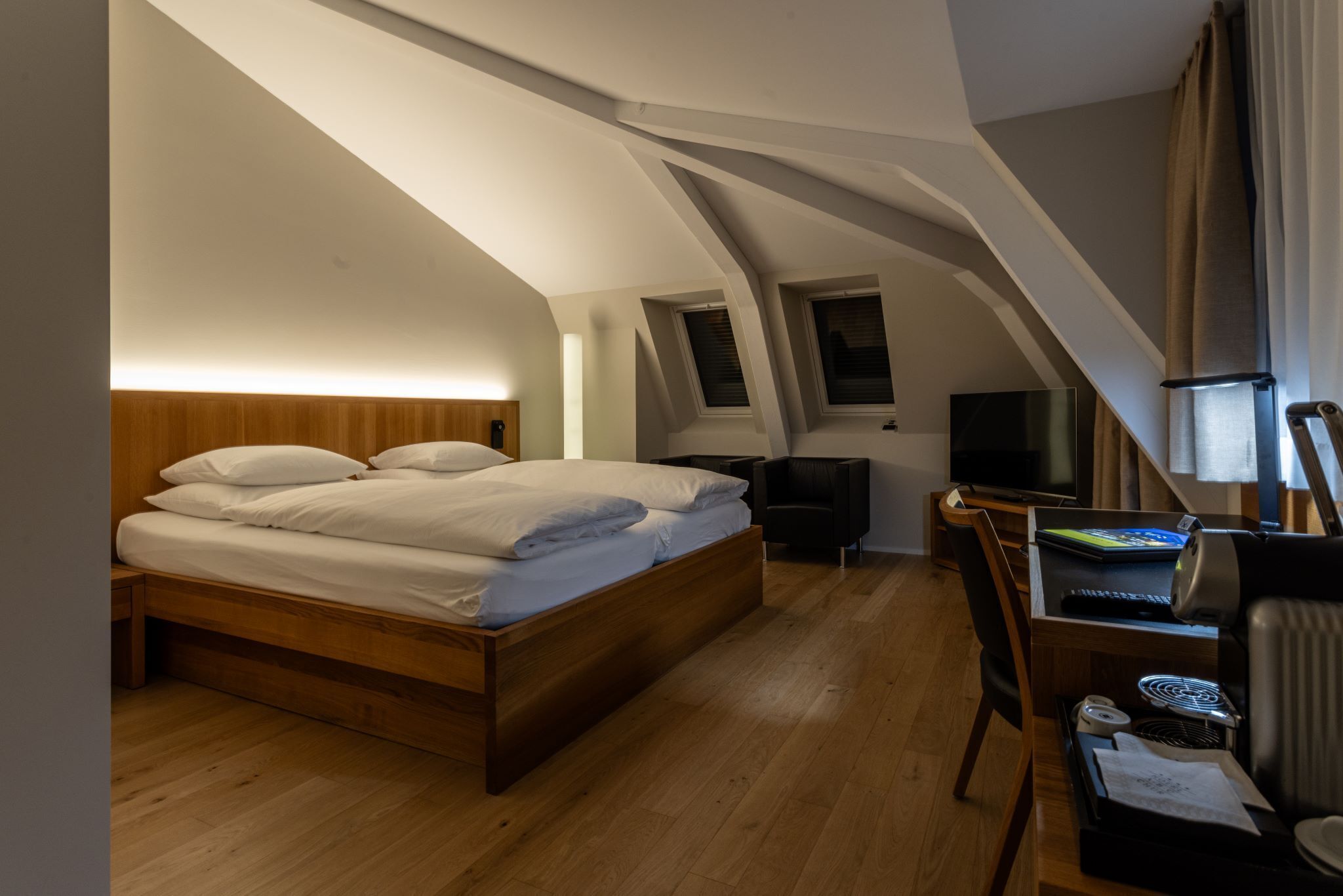 Une chambre à coucher avec un lit en bois, un bureau avec un ordinateur, une télévision et une petite fenêtre.