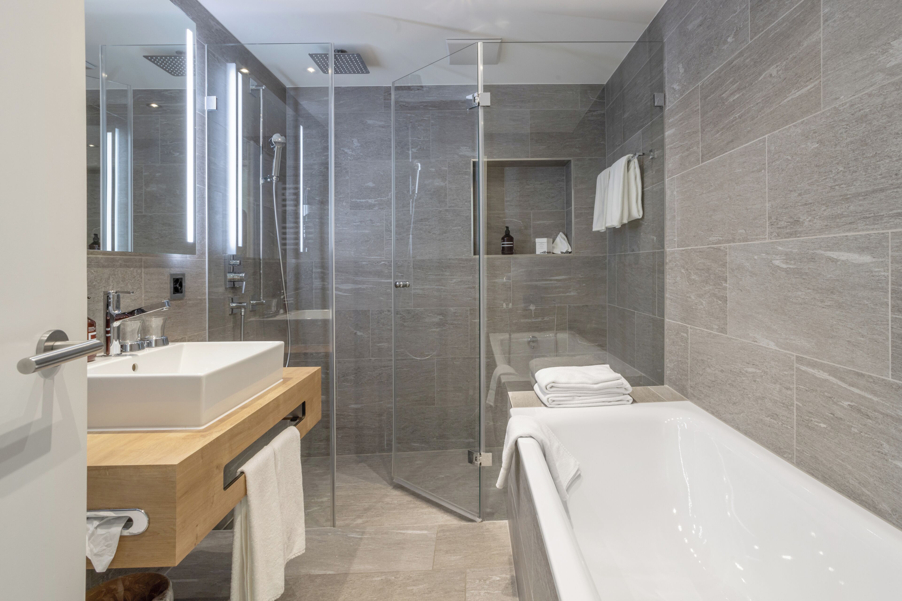 A modern bathroom with a glass-enclosed shower, a bathtub, and a vanity with a sink and mirror.