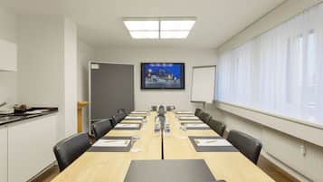 A conference room with a long table, chairs, a projector screen, and a window with curtains.