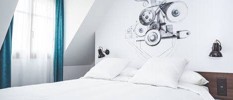 A modern bedroom with a bed, white bedding, a wall-mounted lamp, and a ceiling fan.