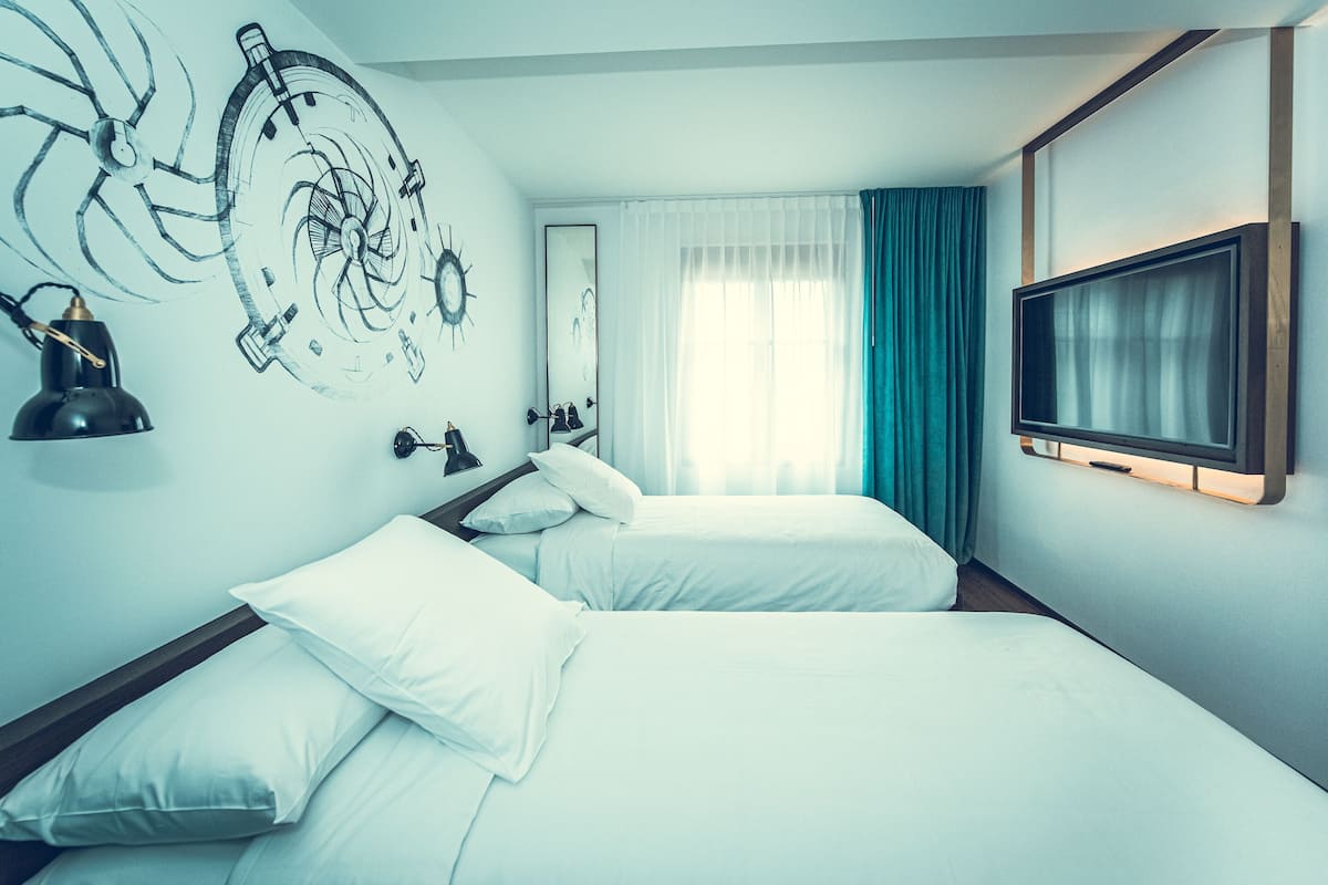 A hotel room with two beds, a large mirror, a television, and a wall mural.