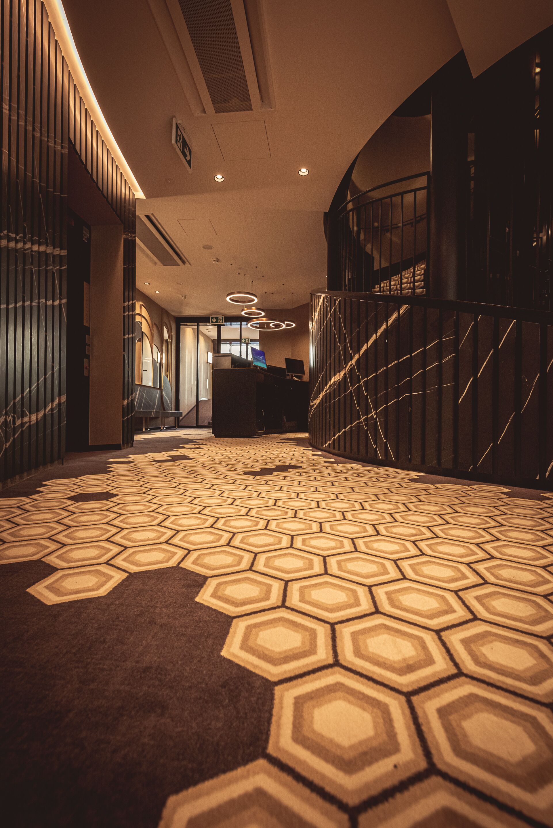 A hotel lobby with a geometric patterned carpet, a reception desk, and a staircase.