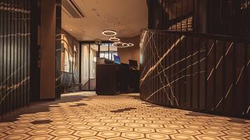 A hotel lobby with a geometric patterned carpet, a reception desk, and a staircase.